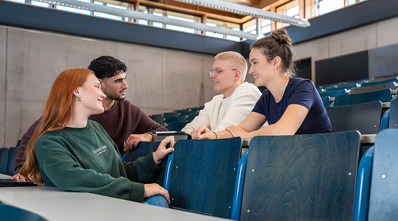 Studentengruppe sitzt im Vorlesungssaal und unterhält sich freundlich miteinander